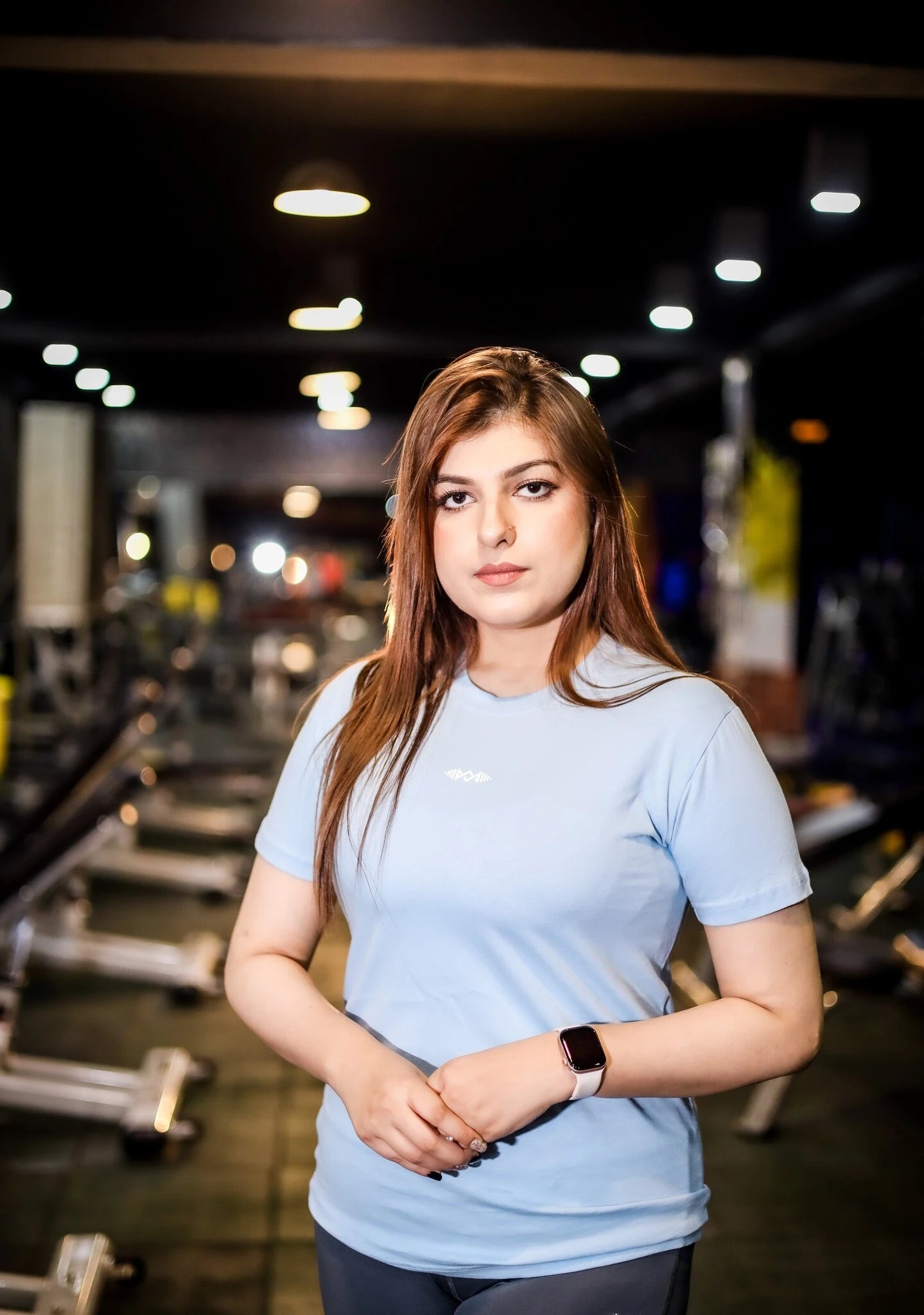 Woman standing in a gym wearing a murks plain light blue t-shirt.